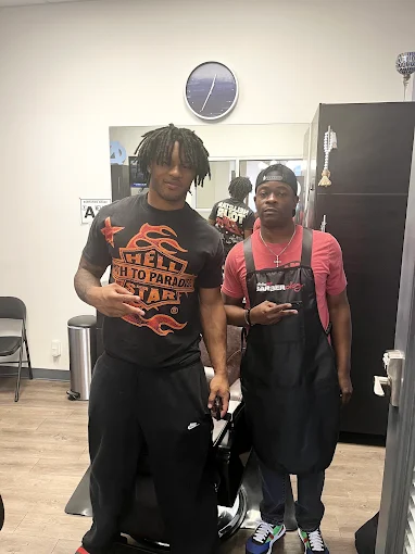 Two men posing inside the barbershop next to a barber chair
