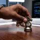 Hands moving a chess piece with IT servers in the background, illustrating CMMC compliance as a GovCon business strategy, not just an IT problem.