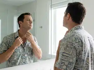 Oahu business man looks at loose neck skin in the mirror. A Honolulu men's neck lift can help tighten skin to improve appearances in Aloha shirt business attire.