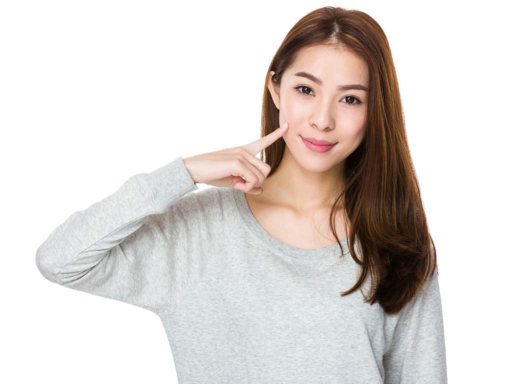 Woman pointing to her cheek dimple. Plastic surgery in Honolulu, Hawaii.