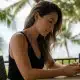 Hawaiian woman on phone searches for the difference between tech neck vs. turkey neck and how a deep plane neck lift or morpheus8 can help.