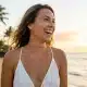 A smiling woman with glowing, youthful skin on a sunny Hawaii beach, representing the natural results of facial rejuvenation at Hawaii Facial Plastic Surgery.