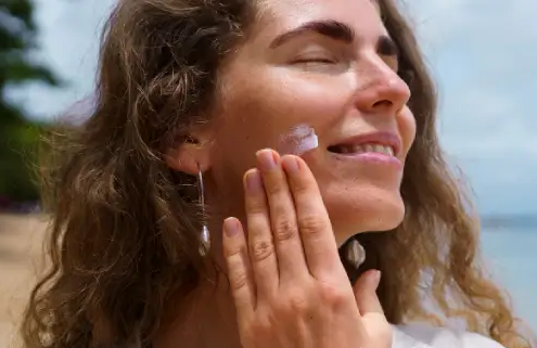 Woman applying sunscreen on a Hawaii beach, protecting her face after surgery with Dr Susan Tan at Hawaii Facial Plastic Surgery.