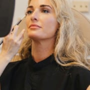 Woman with long blonde hair at the Hawaii Facial Plastic Surgery clinic holds a hand mirror, weighing the results of a natural deep plane facelift for rejuvenation in Honolulu.