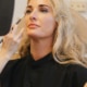 Woman with long blonde hair at the Hawaii Facial Plastic Surgery clinic holds a hand mirror, weighing the results of a natural deep plane facelift for rejuvenation in Honolulu.