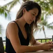 Hawaiian woman on phone searches for the difference between tech neck vs. turkey neck and how a deep plane neck lift or morpheus8 can help.