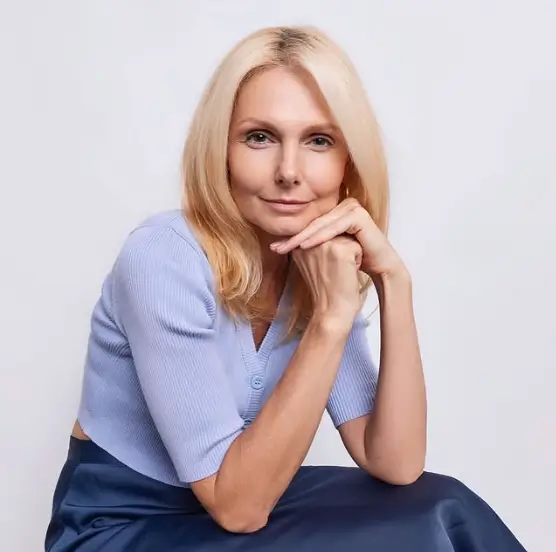 A smiling blonde woman in a light blue top rests her chin on her hands, demonstrating why appearance matters in leadership and first impressions.